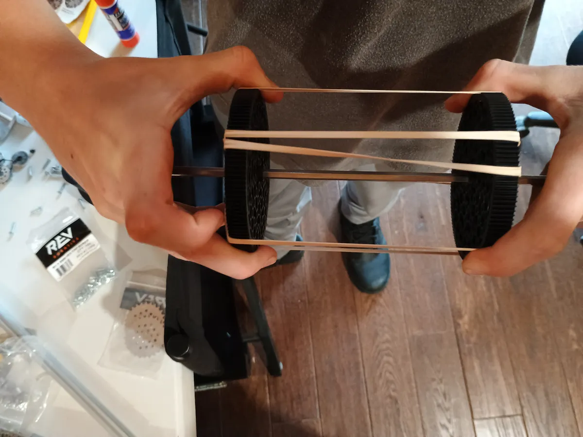 Prototype intake roller: two 3D-printed discs on a shaft with rubber bands stretched between them